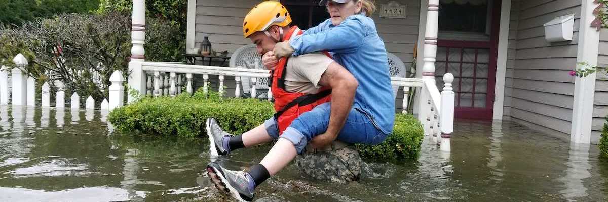 Women riding on back of rescue worker in flooded street outside home