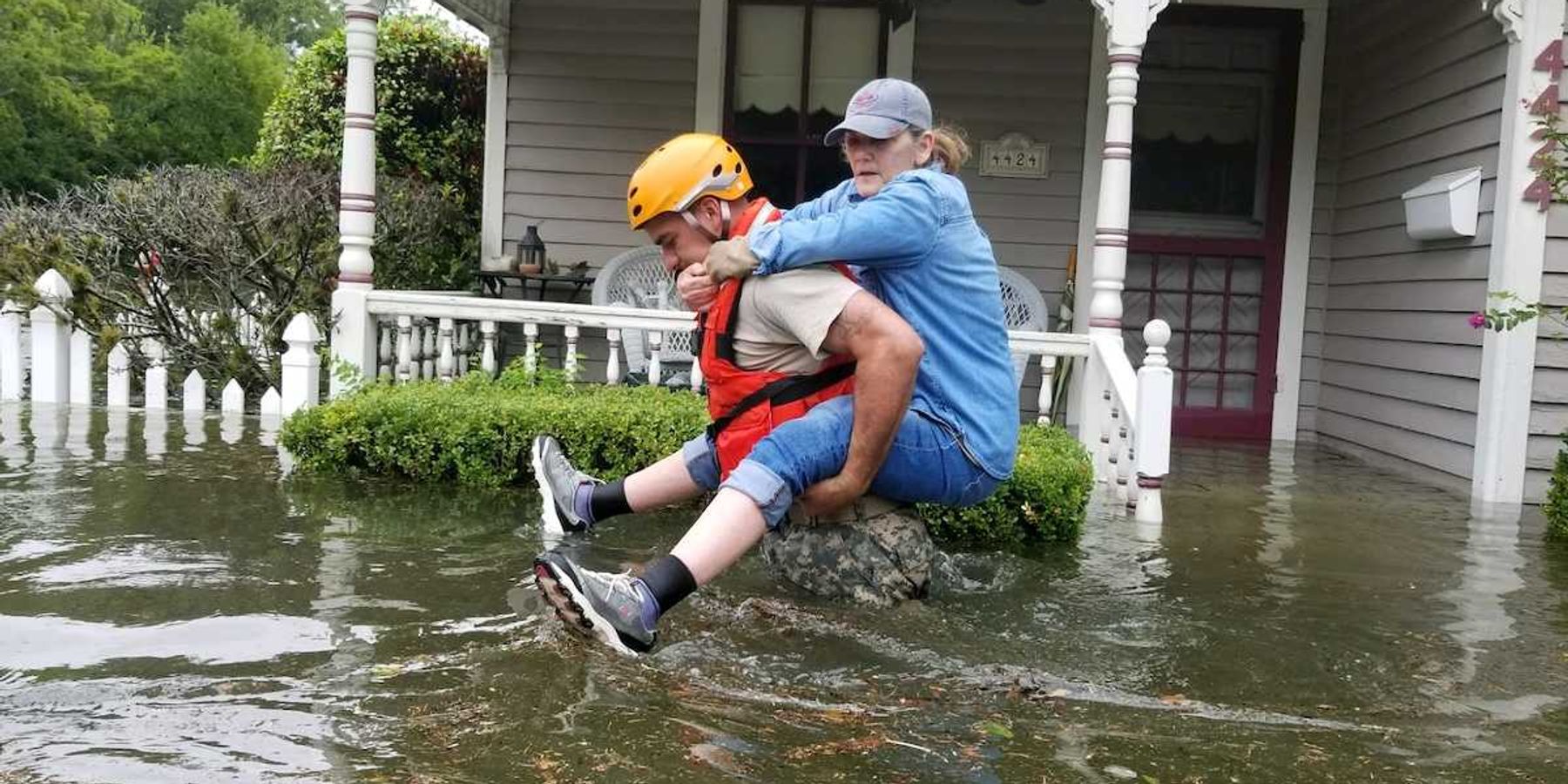 Women riding on back of rescue worker in flooded street outside home