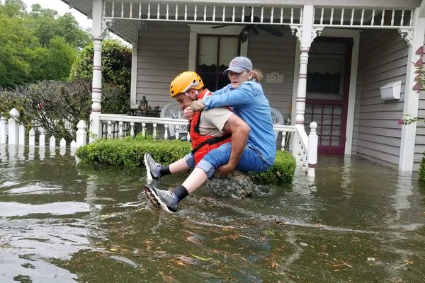 Women riding on back of rescue worker in flooded street outside home