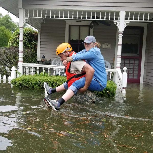 Women riding on back of rescue worker in flooded street outside home