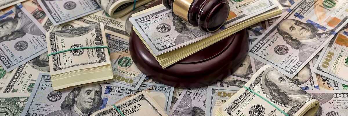 Wooden court gavel overlaying and surrounded by hundred-dollar bills