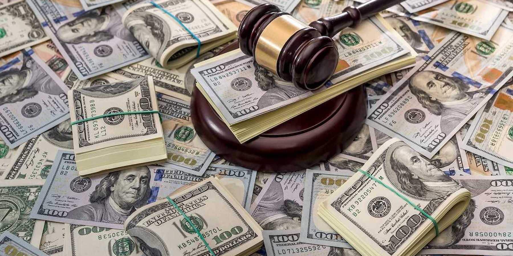 Wooden court gavel overlaying and surrounded by hundred-dollar bills