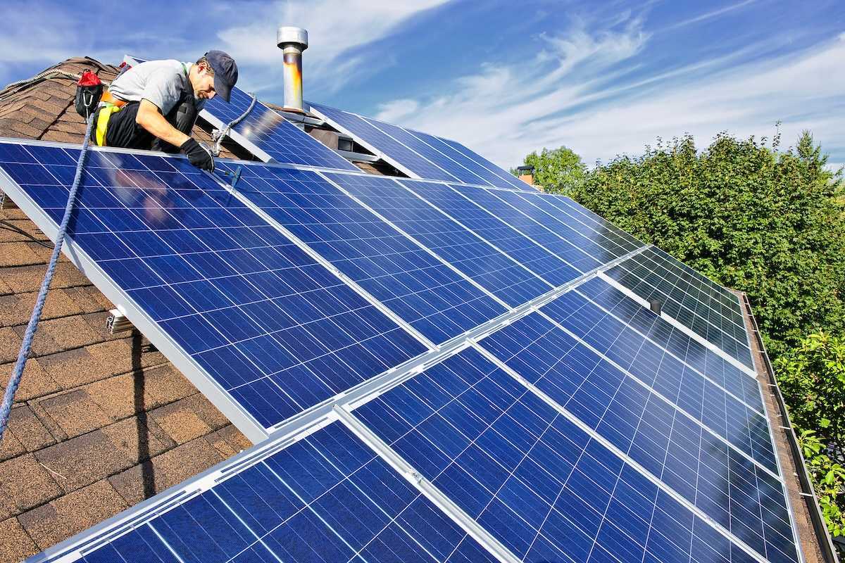 Worker installing solar panels on a shingled residential rooftop