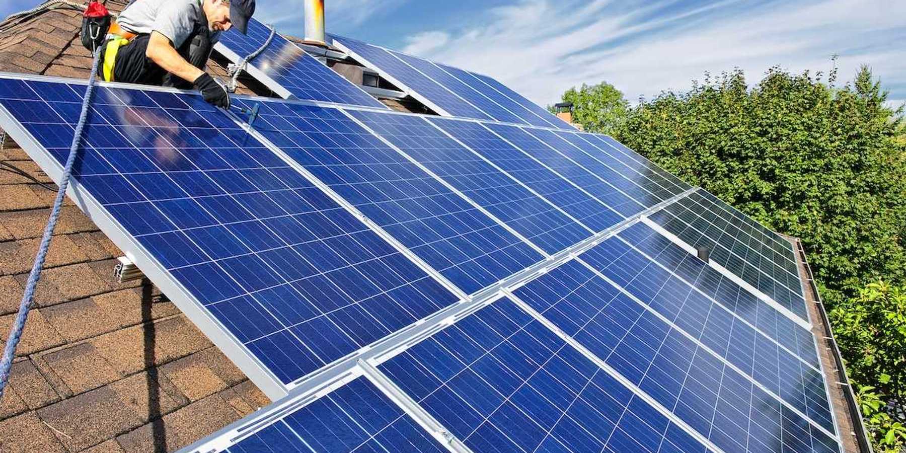 Worker installing solar panels on a shingled residential rooftop