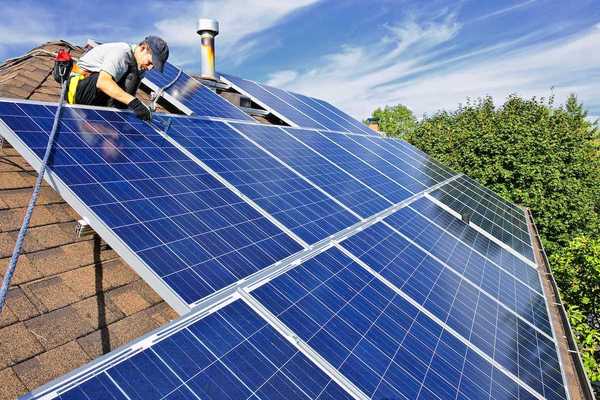 Worker installing solar panels on a shingled residential rooftop