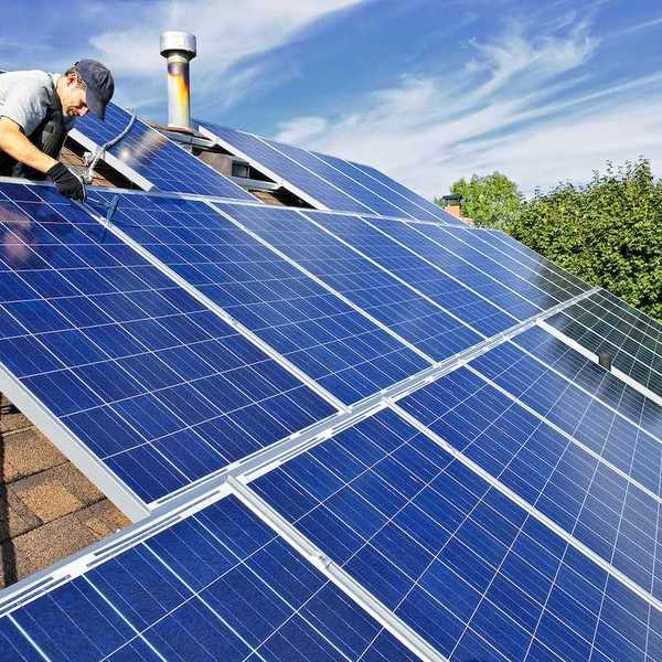 Worker installing solar panels on a shingled residential rooftop