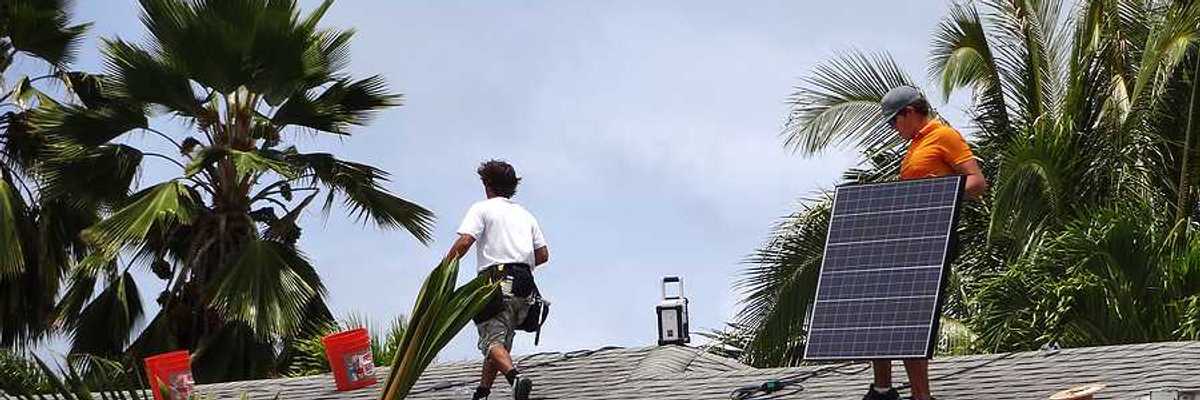 Workers installing solar panels on a roof with palm trees in the background