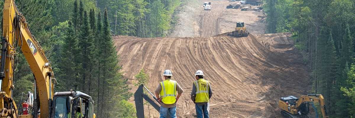 Workers overlook the Enbridge Line 3 Oil Pipeline Construction Site in Minnesota forest with excavators and bulldozer.