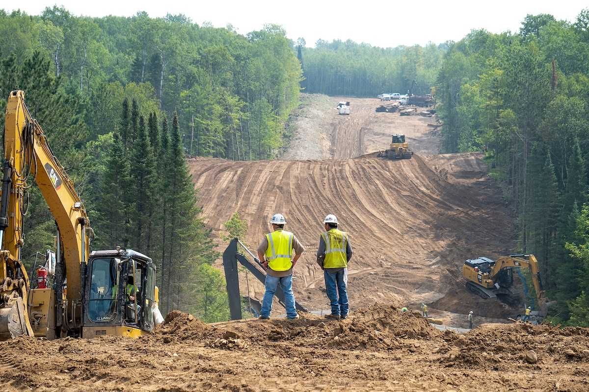 Workers overlook the Enbridge Line 3 Oil Pipeline Construction Site in Minnesota forest with excavators and bulldozer.