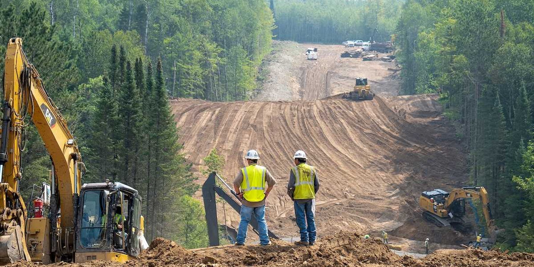 Workers overlook the Enbridge Line 3 Oil Pipeline Construction Site in Minnesota forest with excavators and bulldozer.