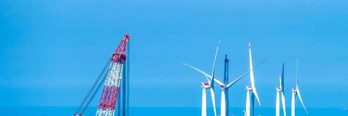 Yellow and white offshore wind turbines being installed using a floating red & white crane