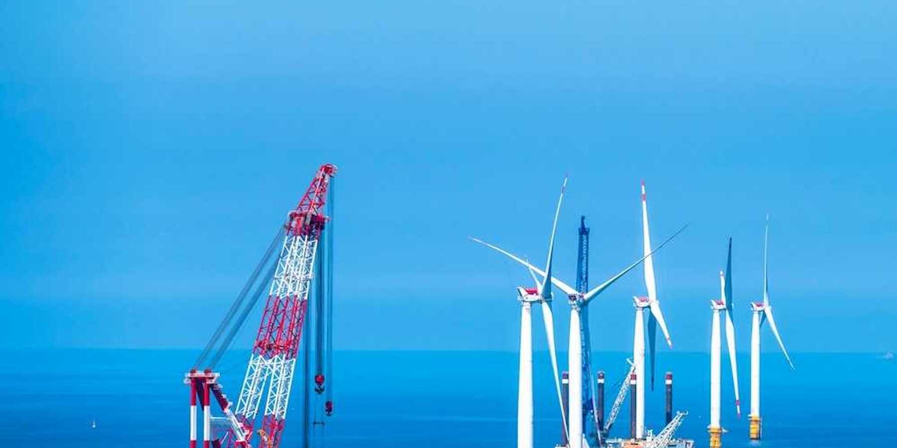 Yellow and white offshore wind turbines being installed using a floating red & white crane