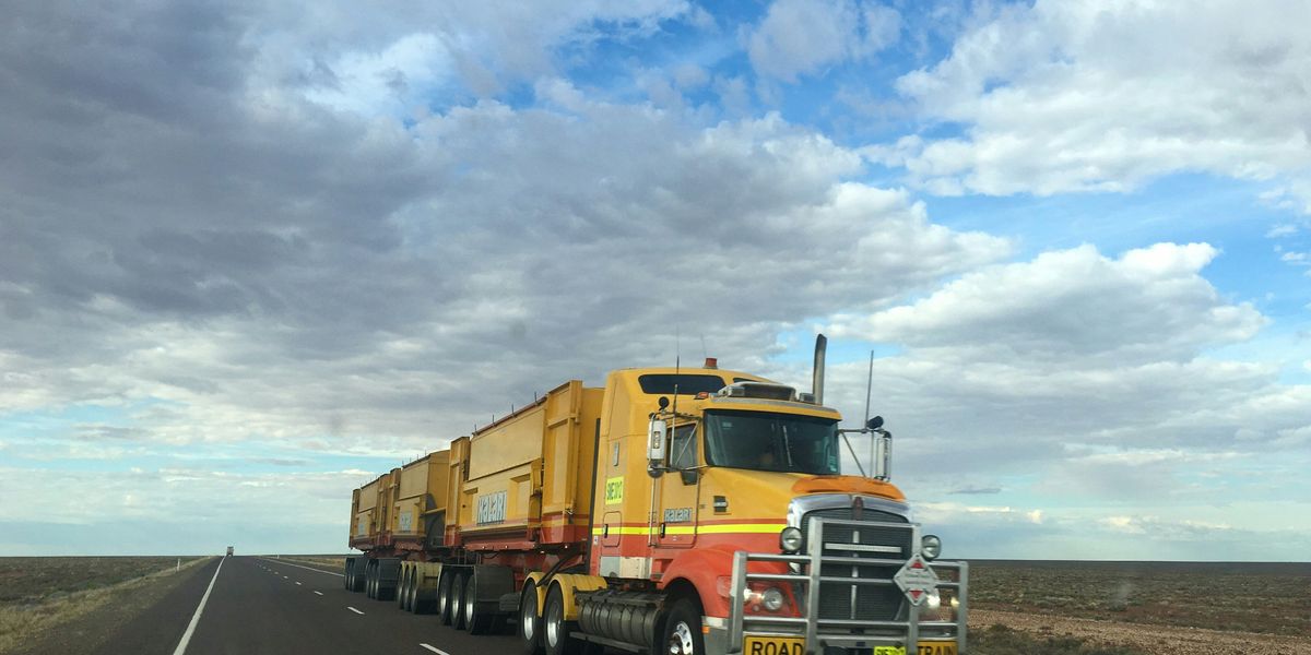 Yellow diesel truck on highway during daytime under partly cloudy skies.