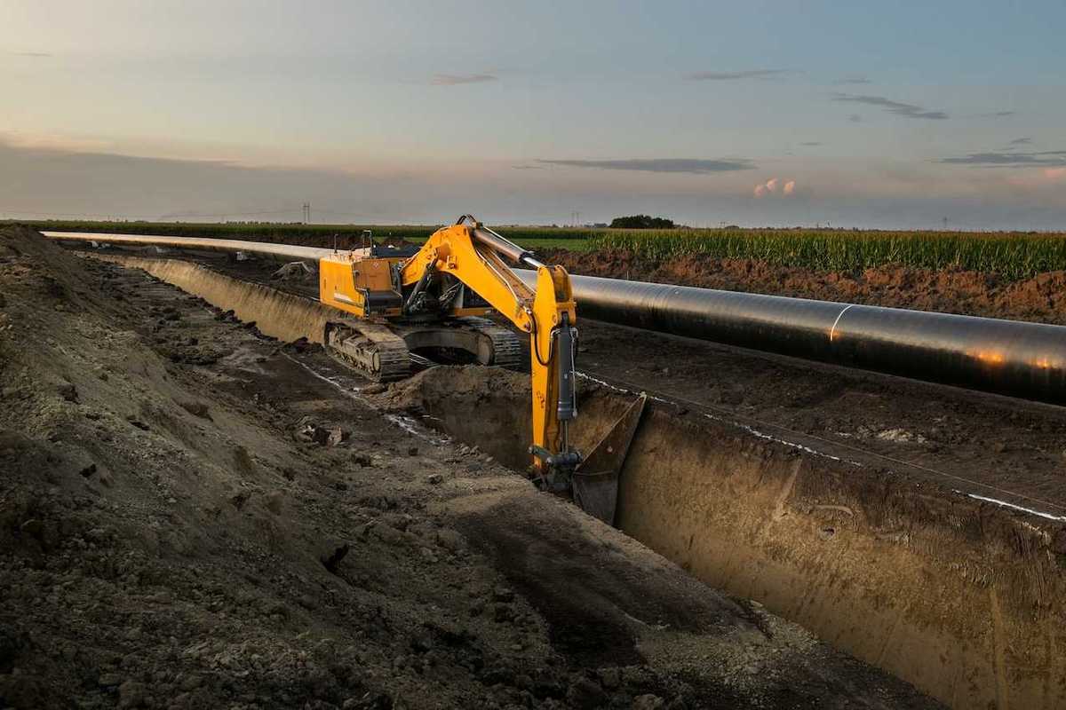 Yellow excavator digging deep trench making way for pipeline construction