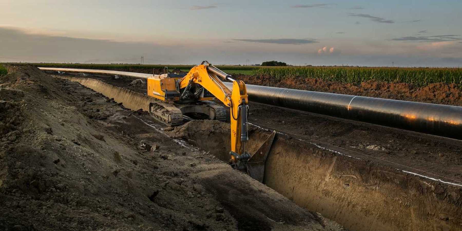Yellow excavator digging deep trench making way for pipeline construction