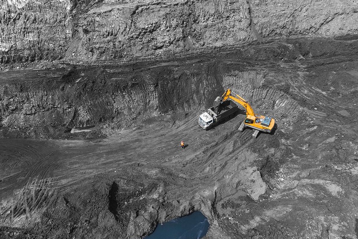 Yellow excavator loading rock truck in open pit coal mine