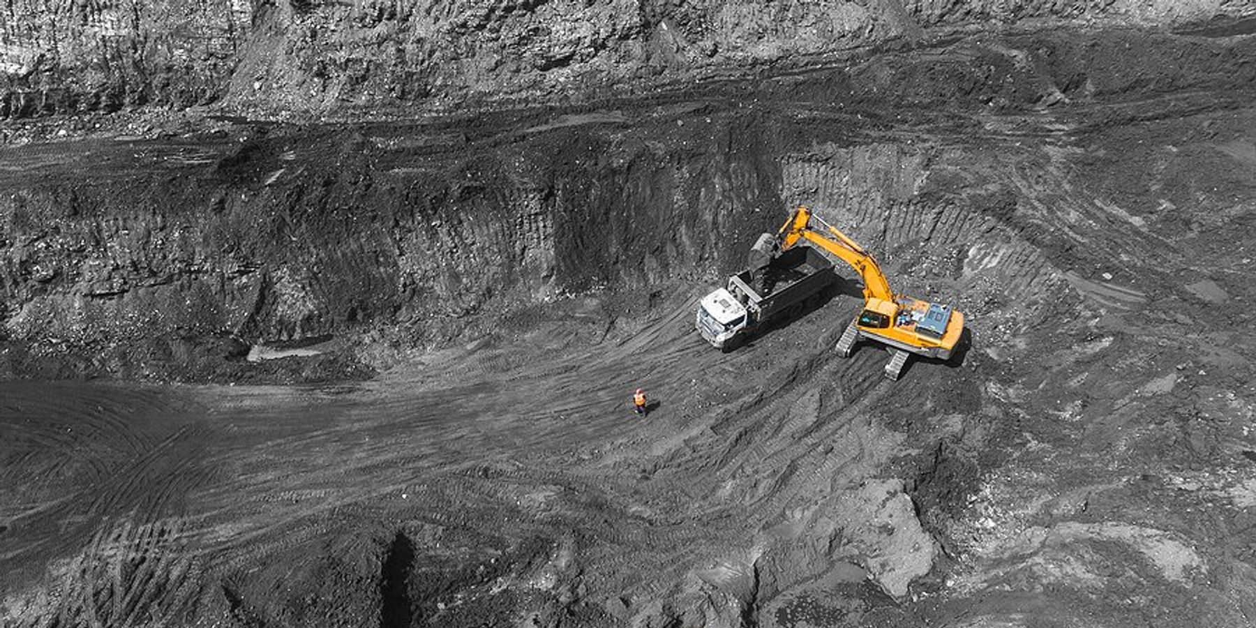 Yellow excavator loading rock truck in open pit coal mine