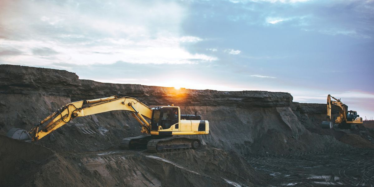 Yellow excavator on an excavated mountain during daytime with sun rising over the horizon.