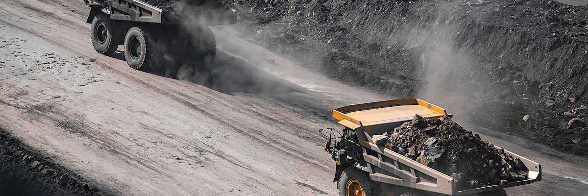 Yellow mining trucks moving along a dusty quarry road while working an open pit coal mine.