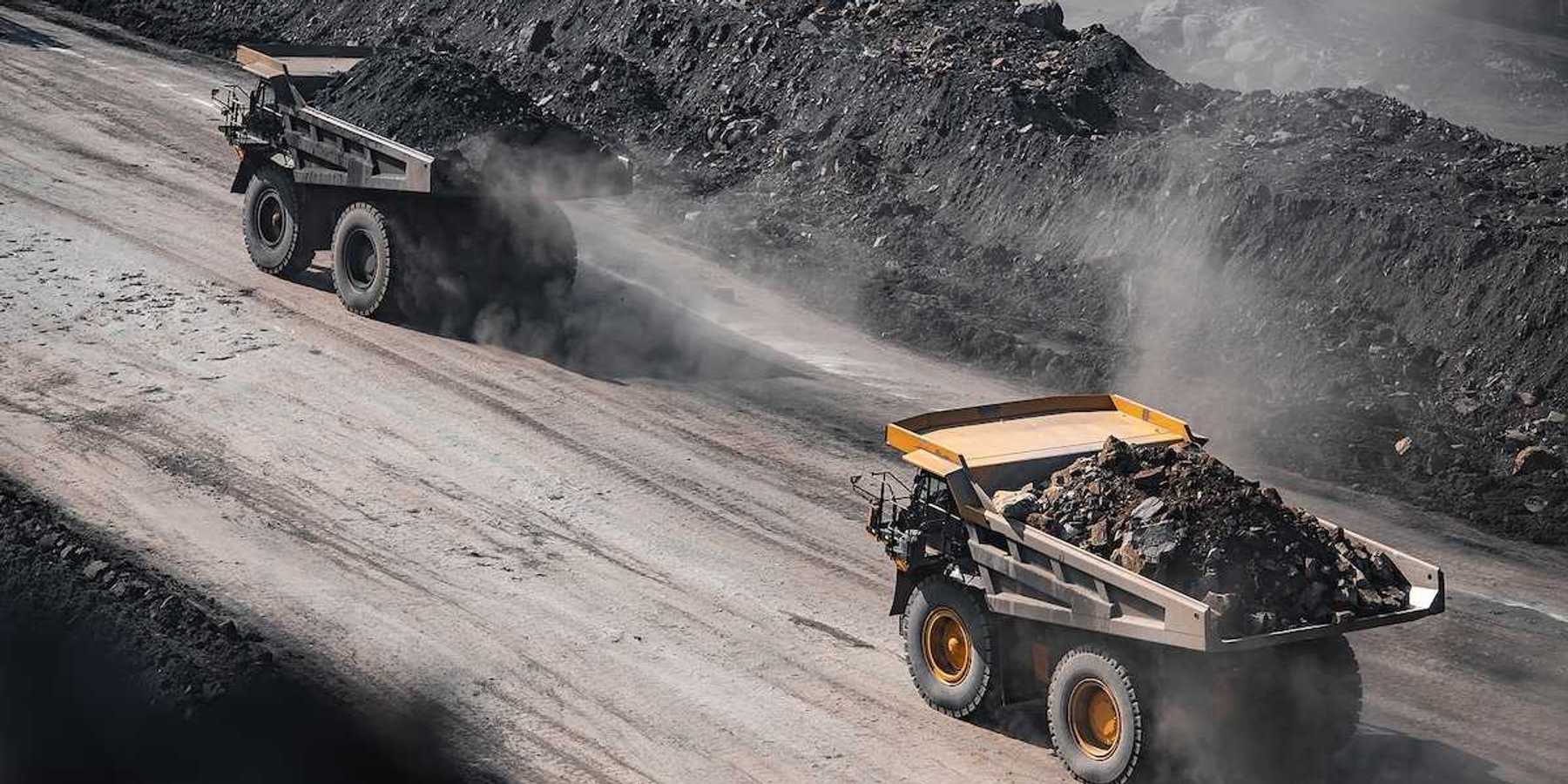 Yellow mining trucks moving along a dusty quarry road while working an open pit coal mine.