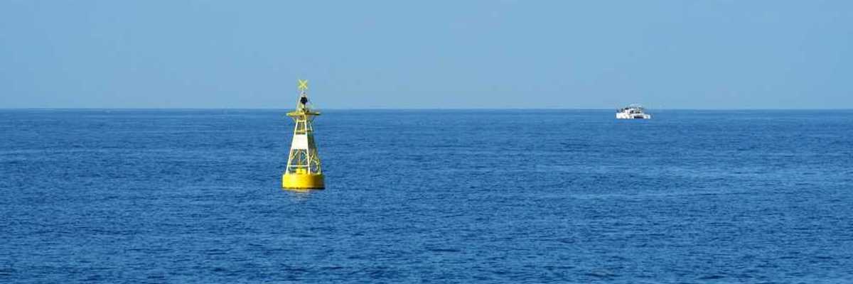 Yellow ocean monitoring buoy with an unidentified white boat nearby