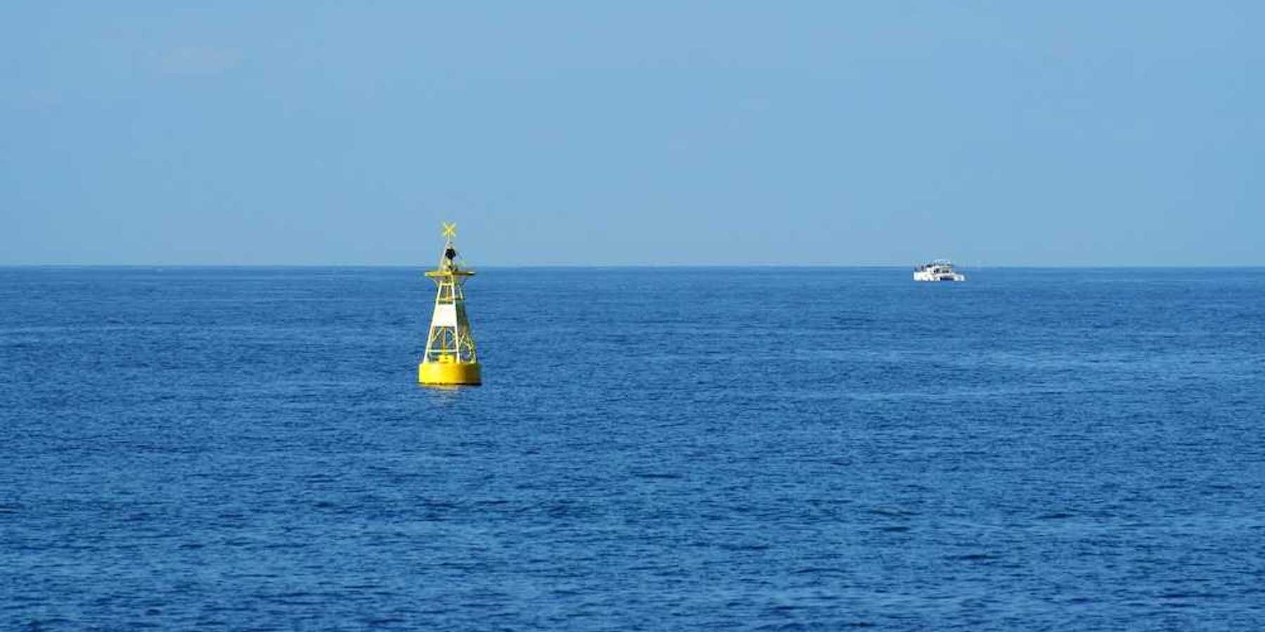 Yellow ocean monitoring buoy with an unidentified white boat nearby