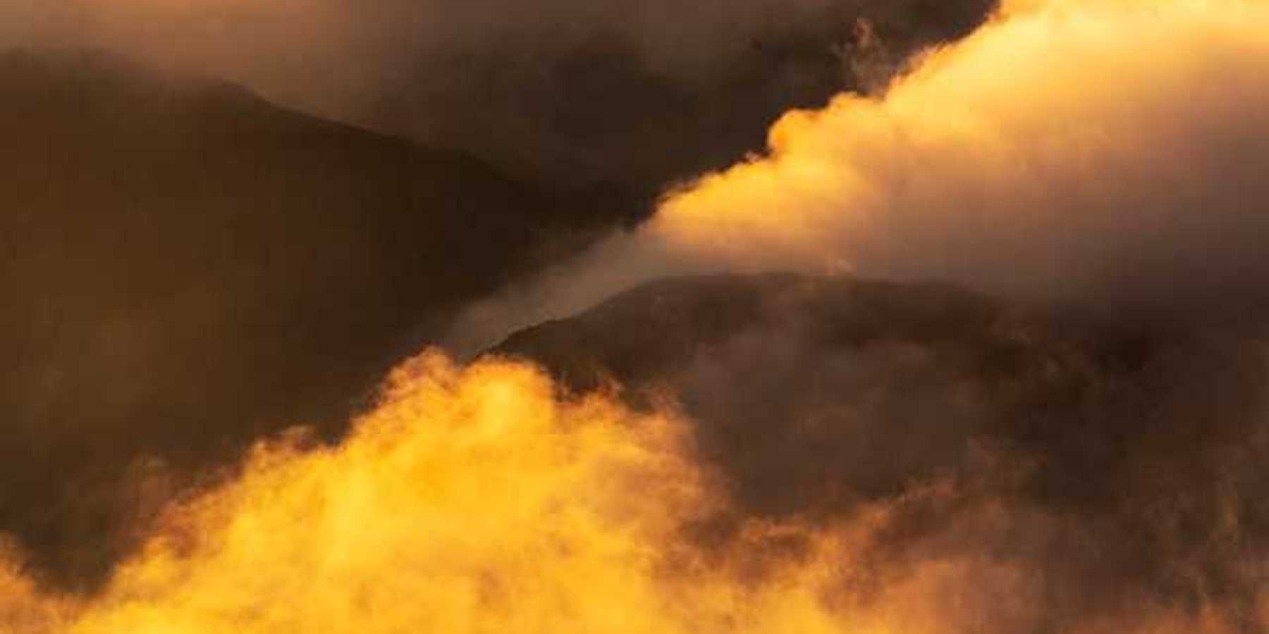 Yellow smoke billowing out of valleys in between mountains