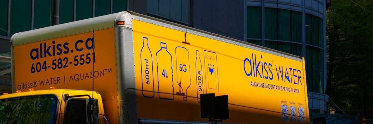 Yellow water delivery truck: "alkiss water. DELIVER TO YOUR DOO"