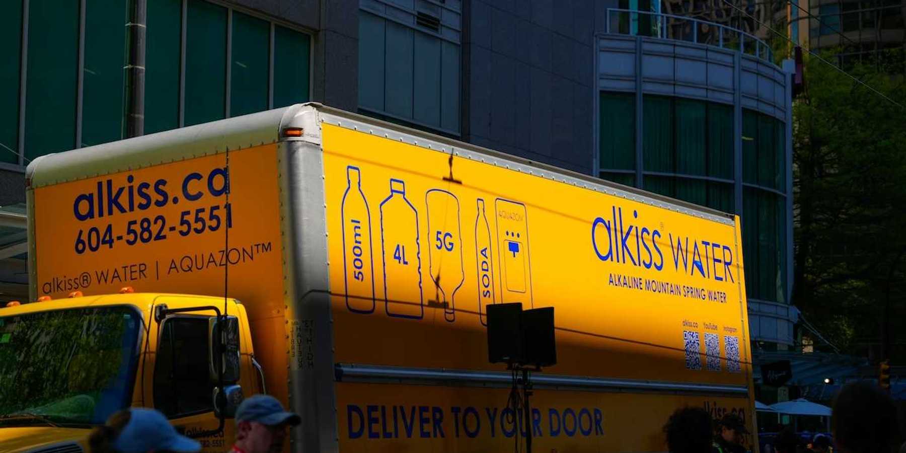 Yellow water delivery truck: "alkiss water. DELIVER TO YOUR DOO"