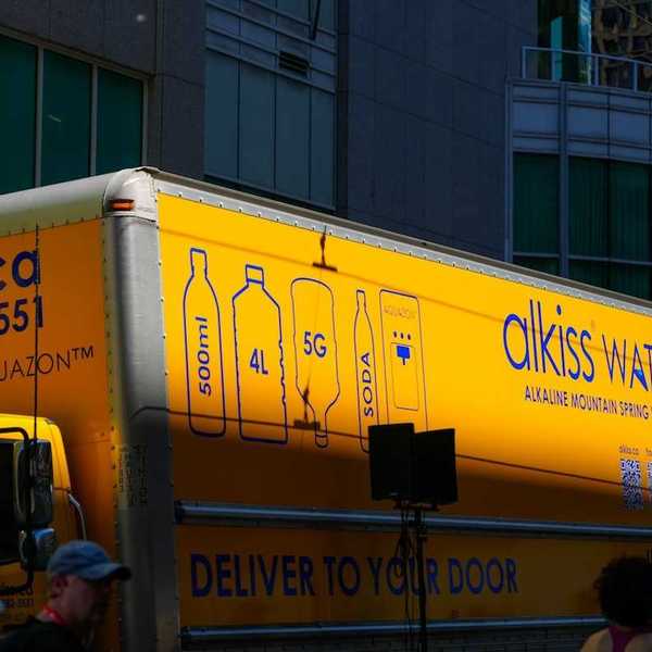 Yellow water delivery truck: "alkiss water. DELIVER TO YOUR DOO"