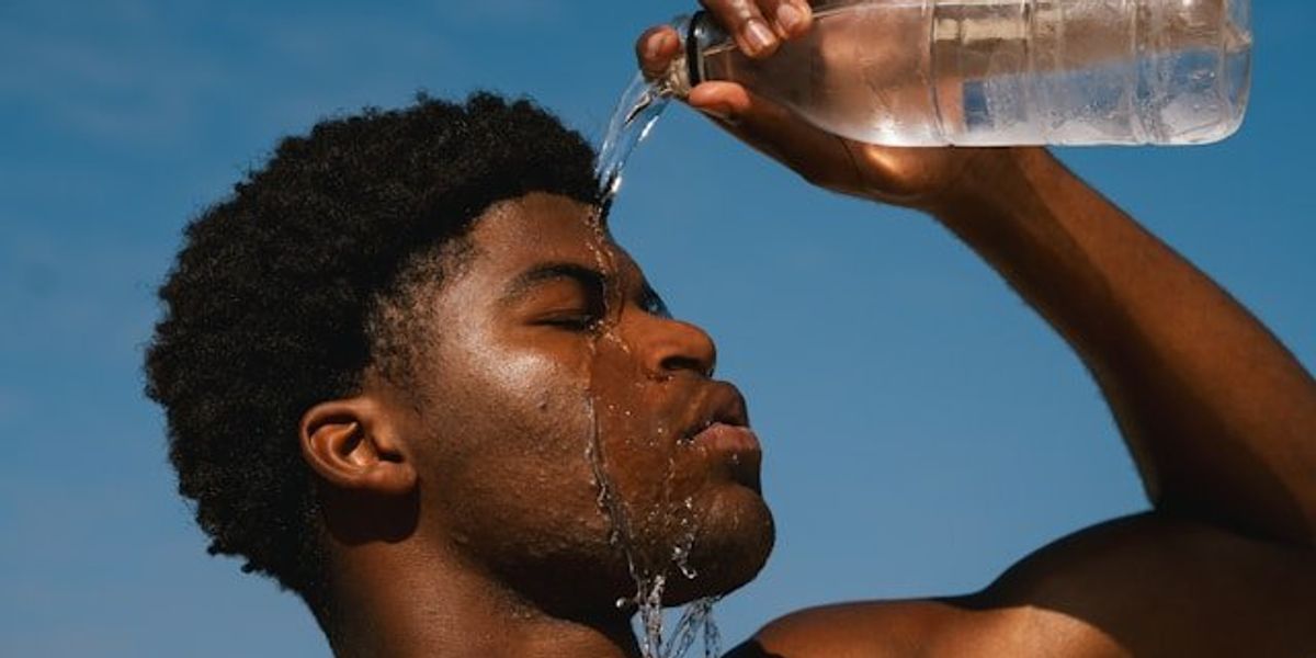 Young Black man pouring a bottle of water on his face on a hot day.