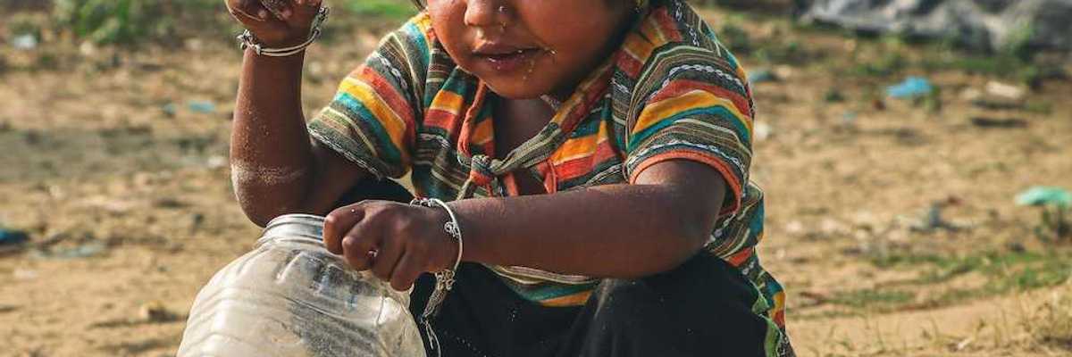 Young child squatting in the dirt, adding coins to a plastic jar