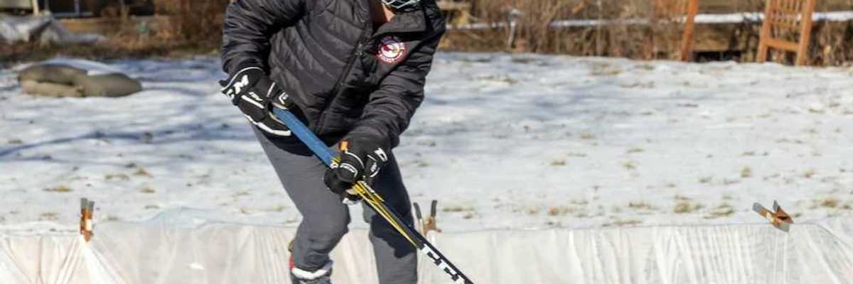 Young person winter-skating on backyard rink with hockey stick and puck