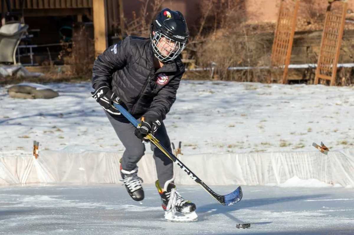 Young person winter-skating on backyard rink with hockey stick and puck