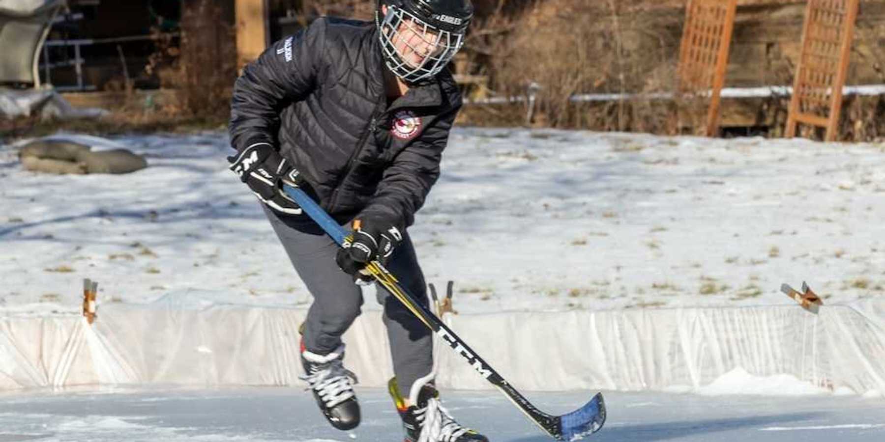 Young person winter-skating on backyard rink with hockey stick and puck