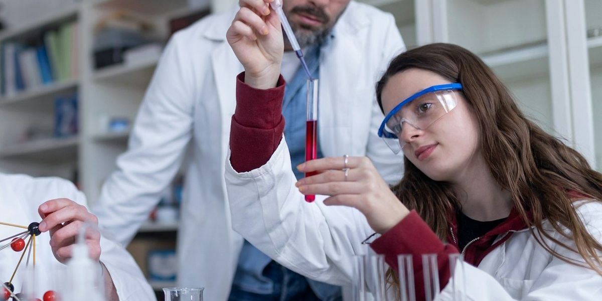 Young scientists and instructor filling test tubes with a red liquid at a lab table.