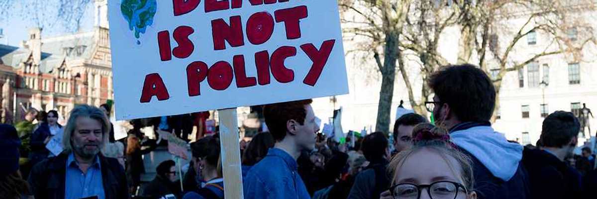 Young woman holding sign of protest reading "DENIAL IS NOT A POLICY."